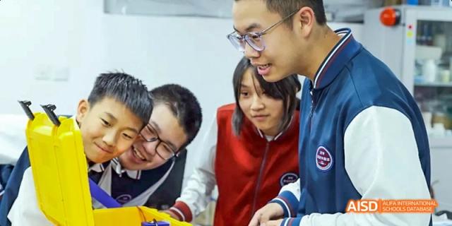 A teacher from Beijing Haidian Foreign Language Academy with a group of students in a classroom or lab.