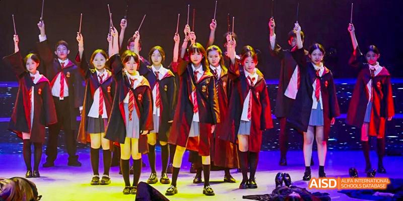 Students from Beijing Haidian Foreign Language Academy on a stage performing a dance or play, with some of them holding what look like wands.