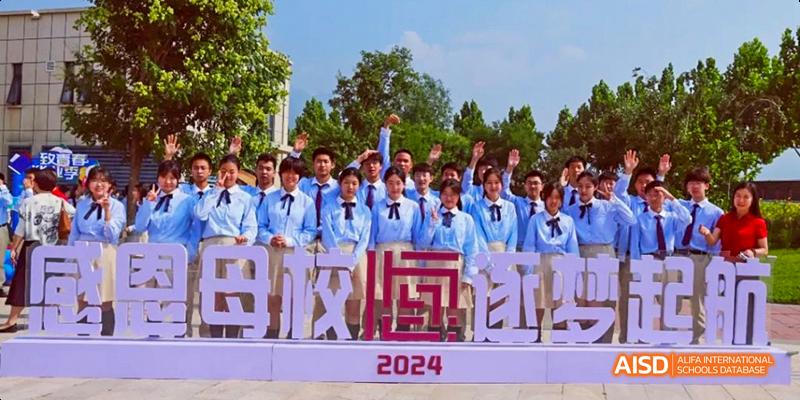A group of high school students from Beijing Haidian Foreign Language Academy in light blue uniforms posing outdoors with a large sign that reads "母校欢迎你" (Welcome to your alma mater) and "2024".