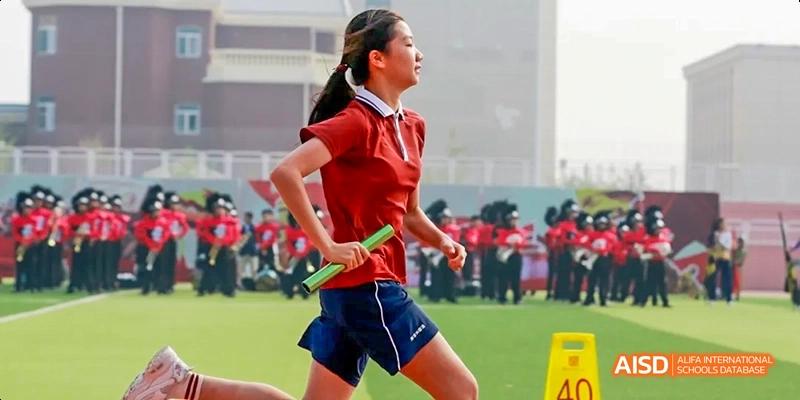 A female student from Beijing Haidian Foreign Language Academy running with a baton during a track and field relay race.