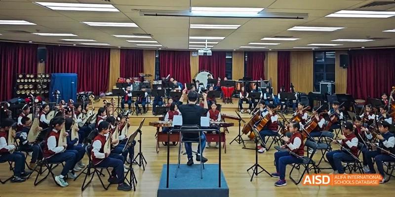 Students from Beijing Haidian Foreign Language Academy performing in an orchestra with a conductor.