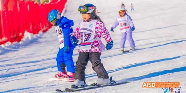 Young students from Beijing Haidian Foreign Language Academy skiing down a snowy hill during a winter sports activity.