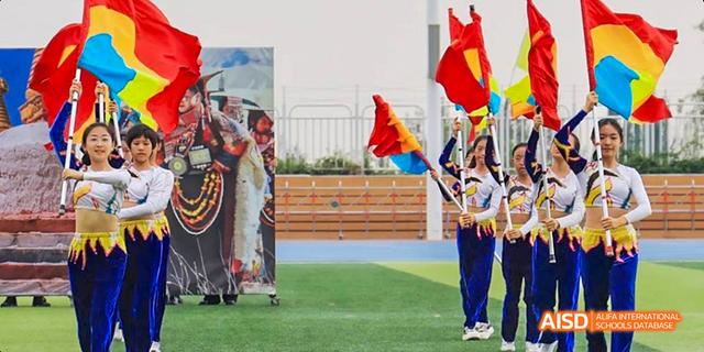 Students from Beijing Haidian Foreign Language Academy wearing traditional attire and waving flags outdoors.