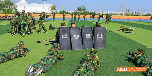 Students from Beijing Haidian Foreign Language Academy participating in military training, with some practicing behind shields on a field.