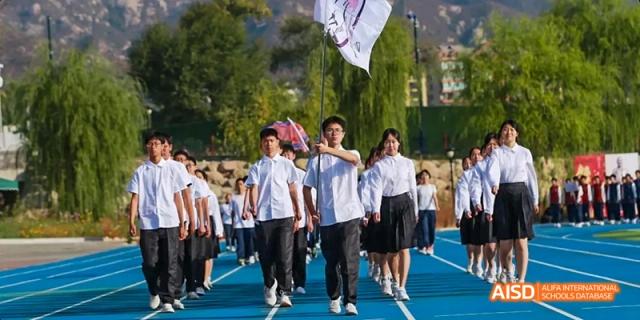 A group of students from Beijing Haidian Foreign Language Academy walking together on an outdoor running track, some carrying flags.