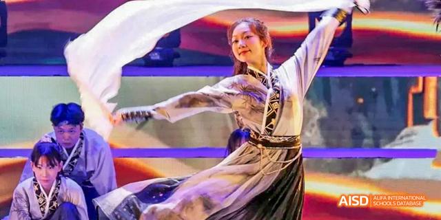 A close-up of a student from Beijing Haidian Foreign Language Academy performing a traditional dance in a white and gold costume.