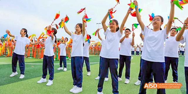 Students from Beijing Haidian Foreign Language Academy cheering and waving flags outdoors in celebration.