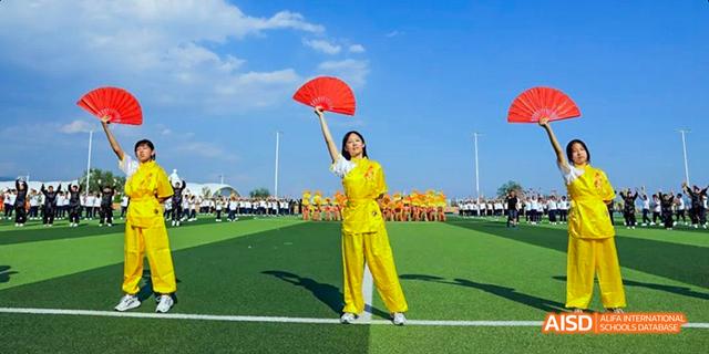 A student from Beijing Haidian Foreign Language Academy in a yellow uniform posing with red fans on a green field.