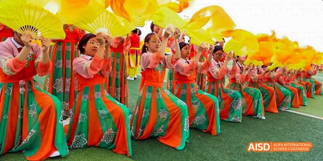 Students from Beijing Haidian Foreign Language Academy performing a lively dance in colorful costumes on a stage.