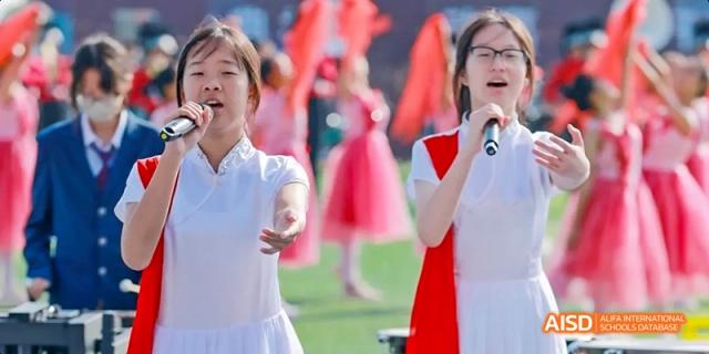 Two female students from Beijing Haidian Foreign Language Academy singing into microphones on a stage.