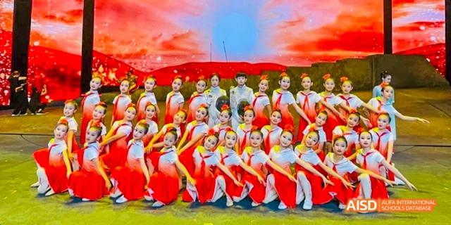 A large group of students from Beijing Haidian Foreign Language Academy in red uniforms posing together on a field after a performance.