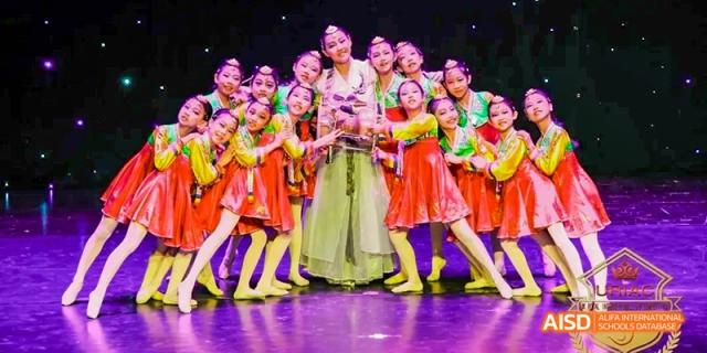 Students from Beijing Haidian Foreign Language Academy posing on a stage in colorful traditional costumes.