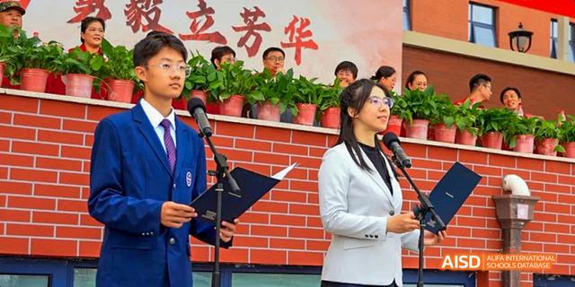 A male and female student from Beijing Haidian Foreign Language Academy speaking at a podium during a school event.