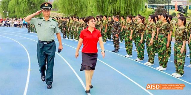 A man and a woman from Beijing Haidian Foreign Language Academy leading a procession of students in military uniforms on a track.