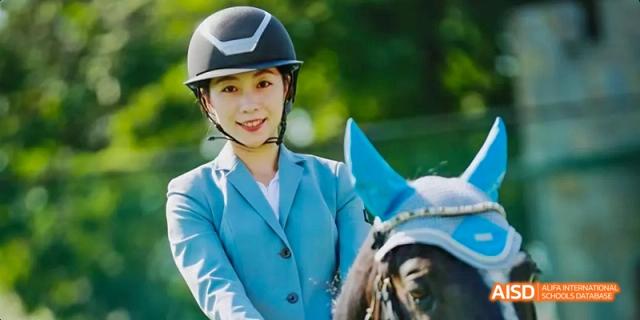 A female student from Beijing Haidian Foreign Language Academy smiling while dressed in riding gear next to a horse.