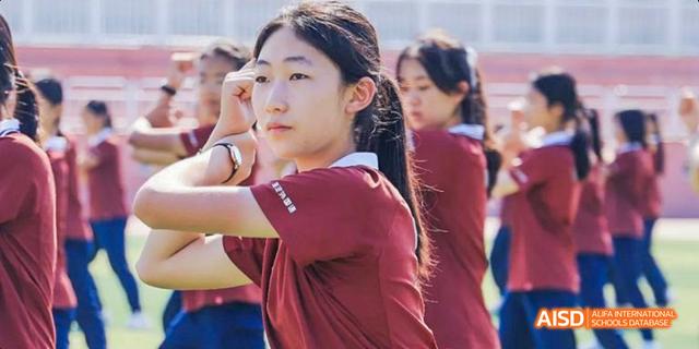 A female student from Beijing Haidian Foreign Language Academy in a red shirt doing a salute during a group activity.