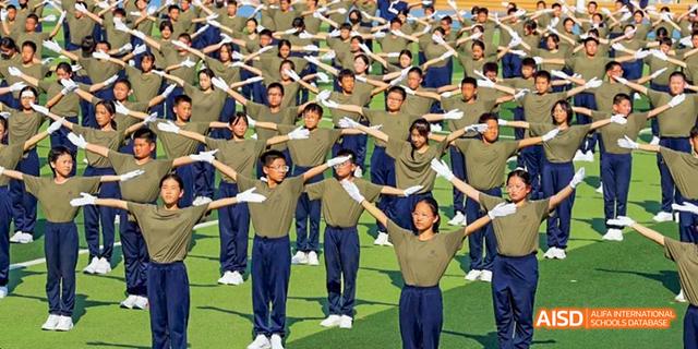 A large group of students from Beijing Haidian Foreign Language Academy performing a synchronized dance or exercise routine on a field.