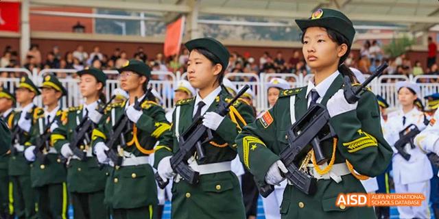 Students from Beijing Haidian Foreign Language Academy in military-style uniforms and holding rifles, marching in a parade.