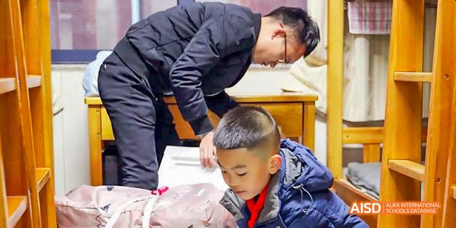 A parent and a male student from Beijing Haidian Foreign Language Academy organizing belongings in a dorm room.
