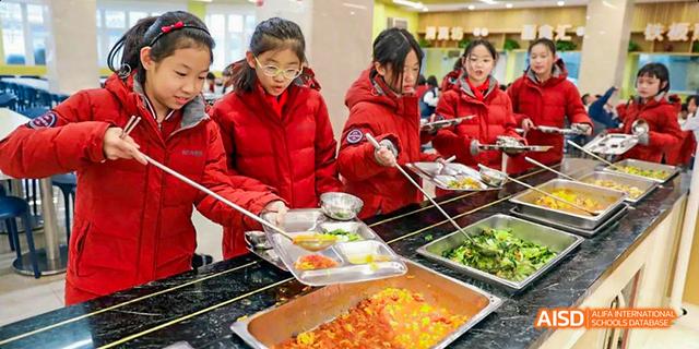 Female students from Beijing Haidian Foreign Language Academy serving themselves from a cafeteria food line.