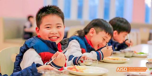 A young boy from Beijing Haidian Foreign Language Academy smiling while eating a meal.
