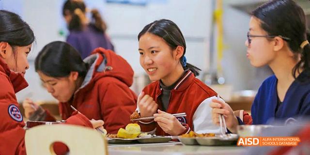 Two students from Beijing Haidian Foreign Language Academy eating together and looking at each other.