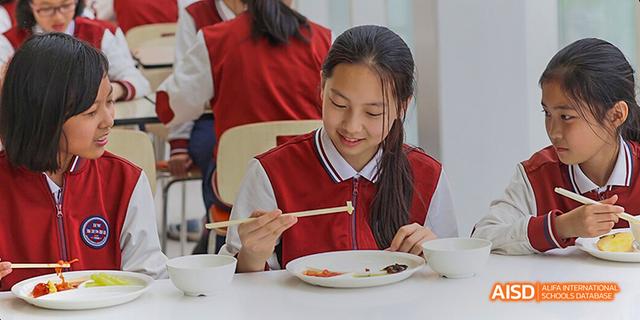 A young girl from Beijing Haidian Foreign Language Academy smiling while eating with chopsticks.
