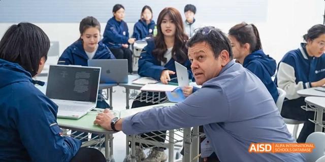 A teacher assisting a student at a computer desk in a classroom at Beijing Hui Xian School.