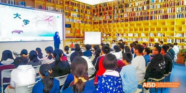 Students sitting on the floor, reading books in a library at Beijing Hui Xian School.
