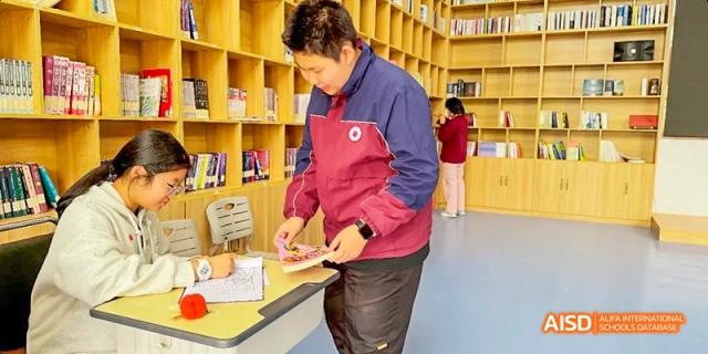A student sitting on the floor of a library, reading a book at Beijing Hui Xian School.