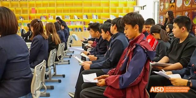 Students sitting at desks with laptops, looking at a screen at the front of the room at Beijing Hui Xian School.