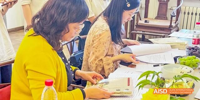A group of people sitting at a table and eating while looking at papers at Beijing Hui Xian School.