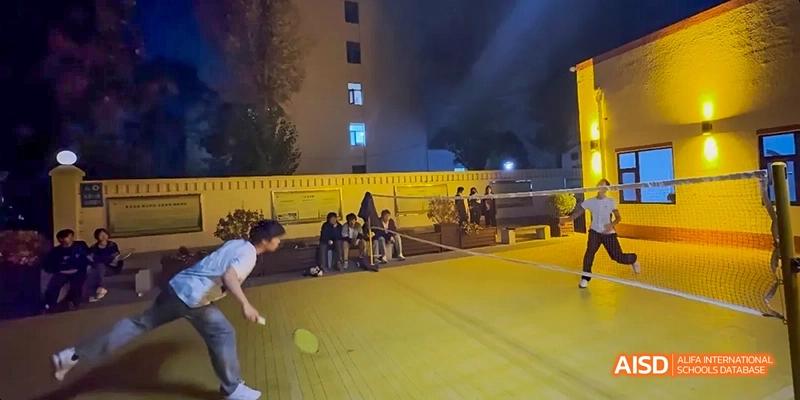A group of students playing basketball on a lit outdoor court at night at Beijing Hui Xian School.