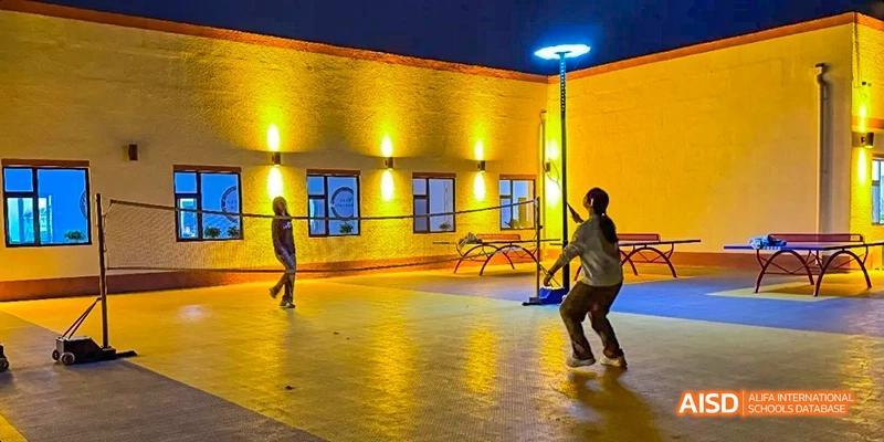 Students playing basketball on an outdoor court at night at Beijing Hui Xian School.