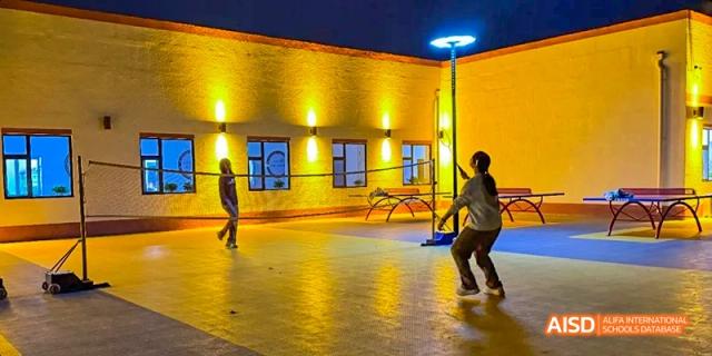 Students playing basketball on an outdoor court at night at Beijing Hui Xian School.