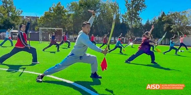 A person practicing with a bow and arrow or doing a stretching exercise on a green field at Beijing Hui Xian School.