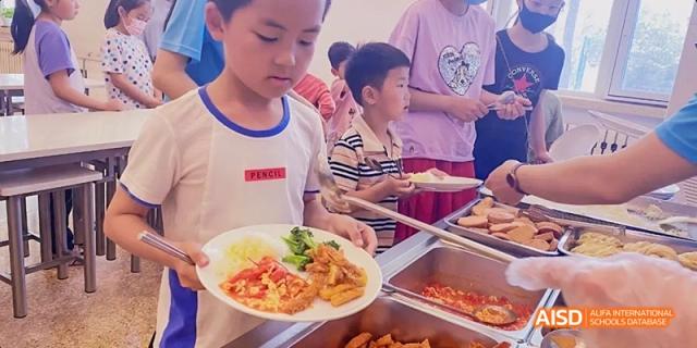 A student serving themselves from a buffet line in the school cafeteria at Beijing Hui Xian School.