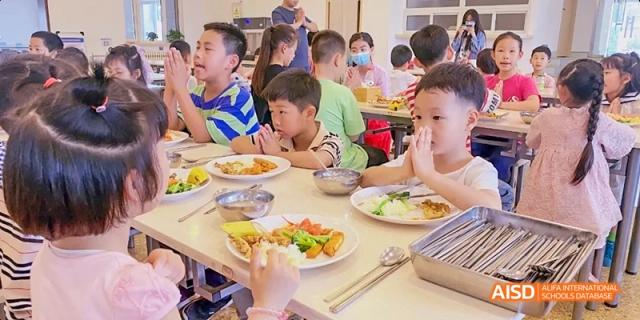 A group of students sitting at a table in the cafeteria, eating lunch together at Beijing Hui Xian School.