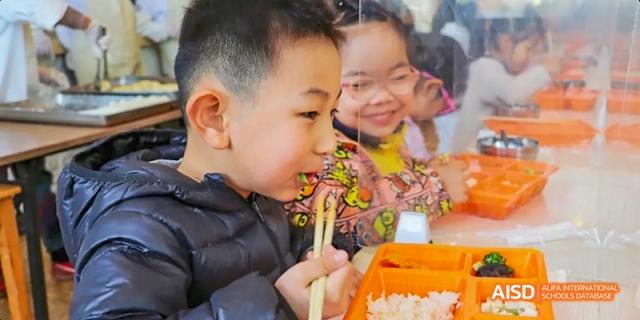 Two young students smiling while eating with chopsticks at Beijing Hui Xian School.