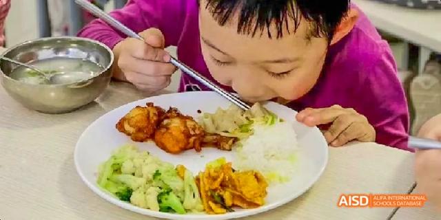 A young child eating a meal from a plate with a fork and spoon at Beijing Hui Xian School.