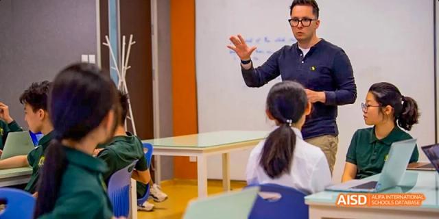 A group of students at Beijing Huijia Private School gather around a teacher who is leading an activity at the front of the classroom.