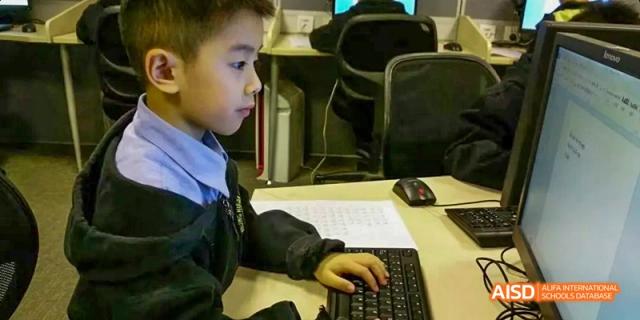 A group of students at Beijing Huijia Private School work together on a project, using a laptop at their desk.