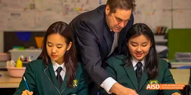 A male teacher at Beijing Huijia Private School stands with two female students, pointing to their work.