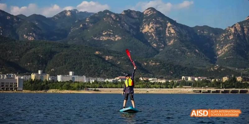 A person at Beijing Huijia Private School paddleboards on a lake with mountains in the background.