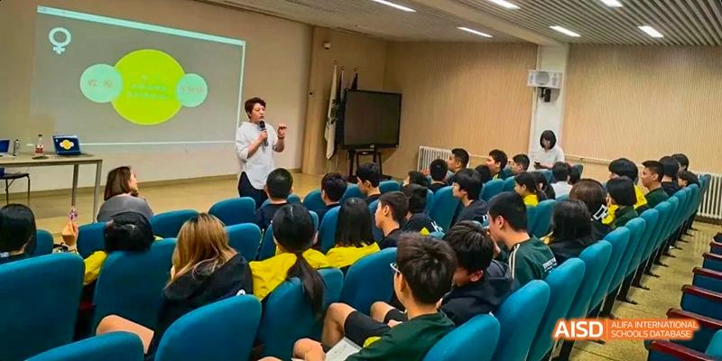 Students at Beijing Huijia Private School are seated in an auditorium, listening to a presentation.