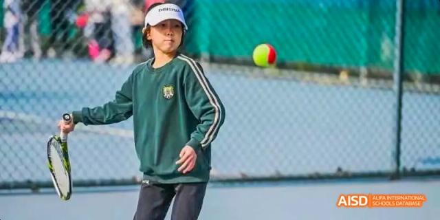 A student at Beijing Huijia Private School in a green uniform throws a ball outdoors.