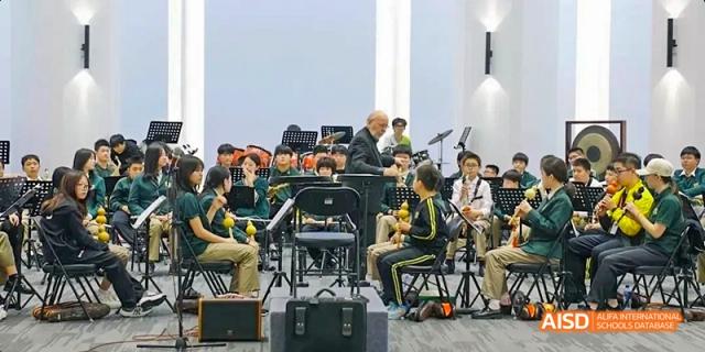 An orchestra of students from Beijing Huijia Private School performs on a stage.