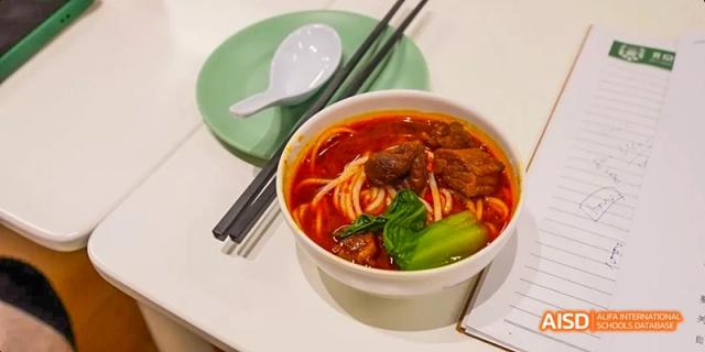 A close-up shot of a bowl of spicy beef noodles with vegetables, a typical dish served at Beijing Huijia Private School.