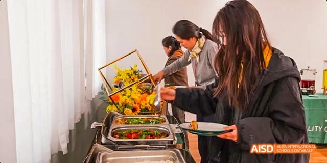 Students at Beijing Huijia Private School serve themselves from a warm buffet table decorated with flowers.