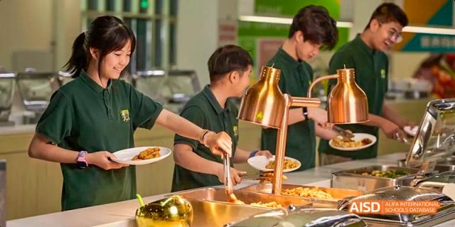 Students at Beijing Huijia Private School wearing green uniforms serve themselves food from a buffet line in the school's canteen.